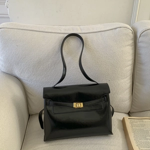 Detail of black glossy leather tote featuring a golden rectangular clasp on a sofa