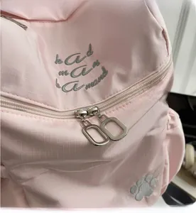 Détail d'un sac à dos rose avec tissu quadrillé, fermetures éclair et broderie