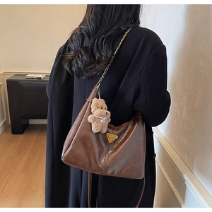 Detail view of the brown hobo bag featuring a metal triangle plaque and plush bear charm