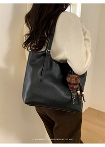 Close-up of black retro leather tote bag with a brown plaid knit hat charm detail