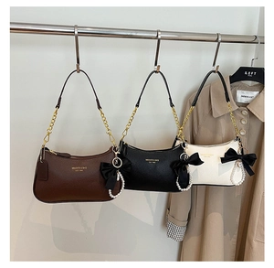 Detalle de bolso chic de axila con cadena dorada y colgante de lazo con perlas