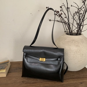 Detail view of a black tote bag featuring a gold metal twist lock on a vintage wooden table