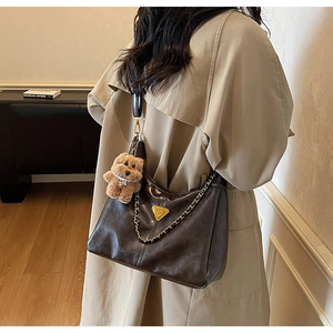 Detail of dark brown leather bag with gold chain and plush bear charm on beige coat