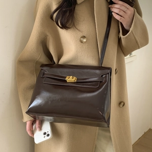 Detail of dark brown leather tote bag with gold swivel lock on a camel wool coat