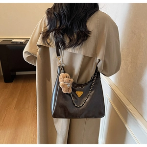 Detail of dark brown leather hobo bag with gold chain and plush bear charm on model
