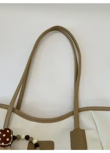 Détail du cabas blanc avec anses en cuir marron et breloque décorative à pois