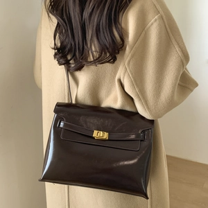 Detail of dark brown glossy leather tote bag with gold metal twist lock on camel coat