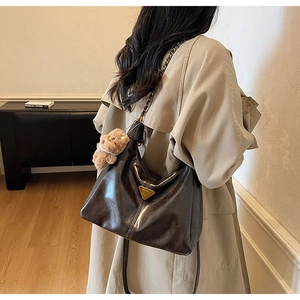 Detail of dark brown glossy leather hobo bag with gold metal logo and plush bear charm