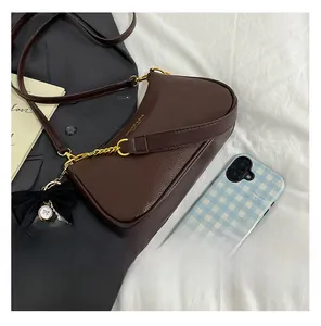 Detalle de bolso de hombro café oscuro con cadena dorada y colgante de lazo con perla