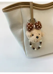 Gros plan d'un bijou de sac ours en peluche avec nœud à pois sur un sac fourre-tout beige