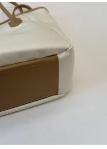 Détail de la base en cuir marron renforcé avec coutures sur le cabas couleur crème