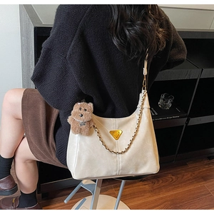 Detail of cream white shoulder bag with gold triangle plate and brown bear charm
