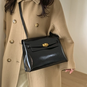 Detail of classic black leather tote bag with gold twist lock on a wool coat