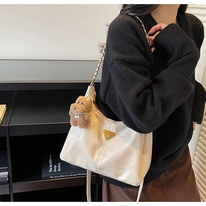 Detail of cream shoulder bag with golden chain and cute brown teddy bear charm accessory