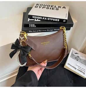 Detalle de bolso de cuero marrón oscuro con cadena dorada y colgante de lazo de perlas