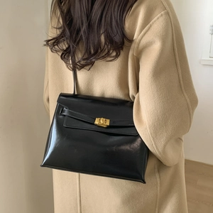 Polished black leather tote bag with gold metal lock buckle styled on beige wool coat