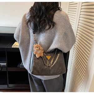 Macro detail of dark grey leather tote with golden triangular logo and chain strap