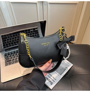 Detalle de bolso negro de cuero granulado con cadena dorada y colgante de perla