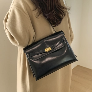 Close-up of a vintage black leather tote bag with a golden square twist lock on a beige coat