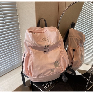 Détail du sac à dos en nylon rose avec broderie grise, poches latérales et fermetures