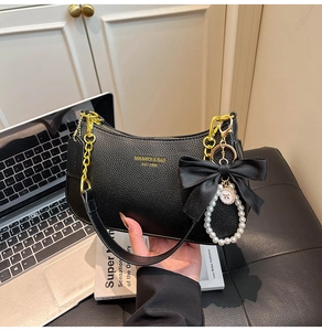 Detalle de bolso hobo de piel negra con logo dorado, cadena y adorno de lazo perla