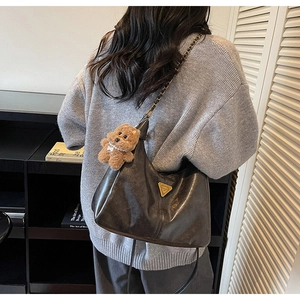 Detail of black faux leather shoulder bag with gold metal logo and brown teddy bear charm