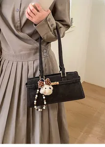 Détail du sac à bandoulière en cuir noir avec serrure dorée et breloque ours