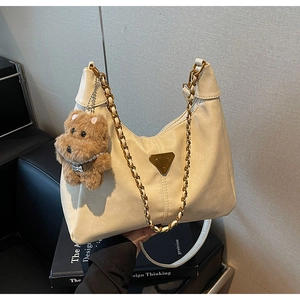 Detail view of cream leather underarm bag with gold chain and teddy bear charm accessory