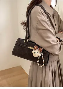 Détail du sac Boston en daim marron foncé avec breloque chiot en peluche et boucle rétro