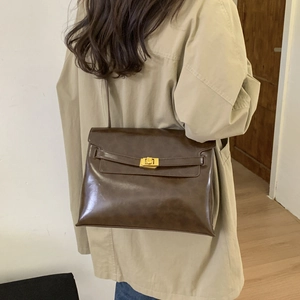 Detail view of brown vintage leather tote bag with gold buckle on a beige trench coat