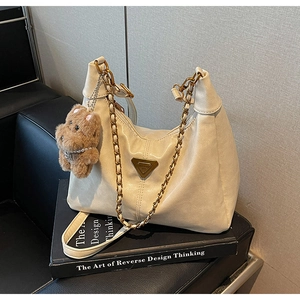 Detail of cream shoulder bag featuring gold triangle plaque and plush bear charm