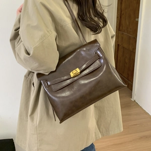 Detail of dark brown leather handbag with gold twist lock on a khaki trench coat