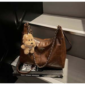 Detail of dark brown leather shoulder bag with gold chain and plush bear charm on books