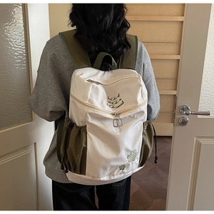 Détail du sac à dos en toile montrant le patchwork beige et vert olive brodé