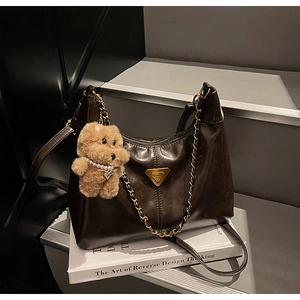 Close-up of a glossy dark brown half-moon bag with gold chain and teddy bear charm