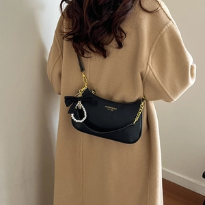 Detalle de bolso media luna negro con cadena de perlas y lazo de terciopelo en abrigo