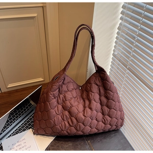 Close-up of burgundy quilted tote bag with silver snap button on a wooden office desk