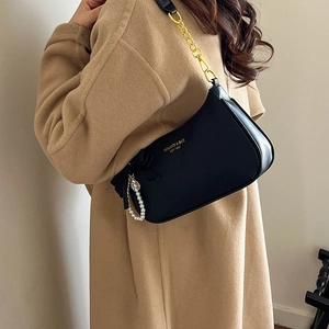 Detalle de bolso en cuero negro con lazo de seda, perlas y cadena dorada sobre abrigo