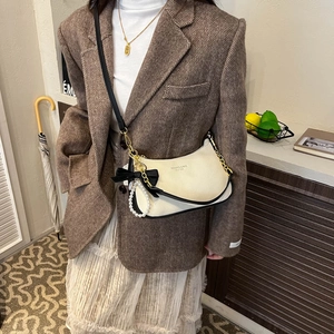 Detalle de bolso de cuero blanco roto con lazo negro, cadena de perlas y colgantes vintage
