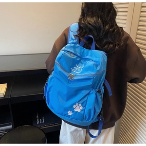 Détail d'un sac à dos bleu en nylon avec broderie de pattes et poches latérales à cordon