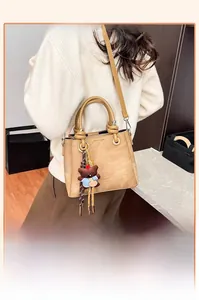 Detail of beige leather bucket bag with knot handle and cute teddy bear charm
