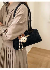 Détail d'un sac Boston en daim noir avec fermoir doré et charm d'ours en peluche