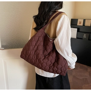 Detail of burgundy quilted puffer tote bag featuring diamond stitching and metal snap closure