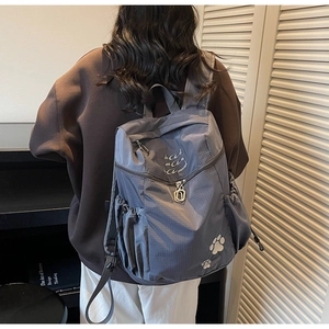 Détail d'un sac à dos à carreaux bleu-gris avec broderie blanche et poche latérale