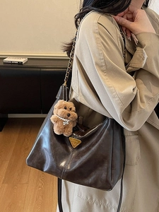 Brown leather hobo bag with gold chain strap and teddy charm worn by a model in a trench coat