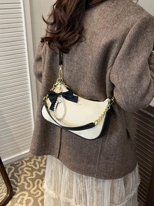 Elegante bolso de hombro en cuero crema con lazo negro y perla mostrado en una modelo