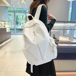 Detail of white star-patterned backpack featuring a front zipper and plush ball charm