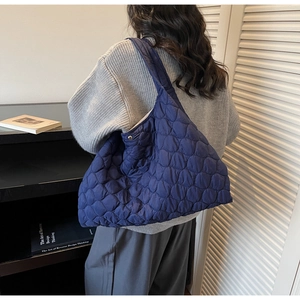 Detail view of navy blue quilted puffer tote bag with shell patterns on a model