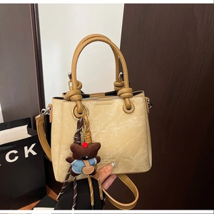 Detail of beige lychee pattern bucket bag with knot handle and cute brown bear charm
