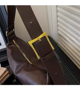 Detail of dark brown leather tote featuring a premium gold rectangular buckle and zipper